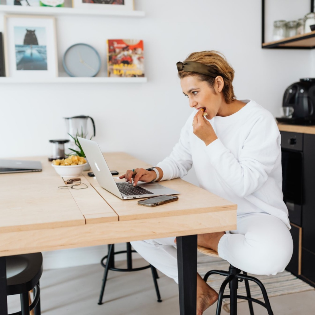 woman sitting at table and looking at laptop while snacking